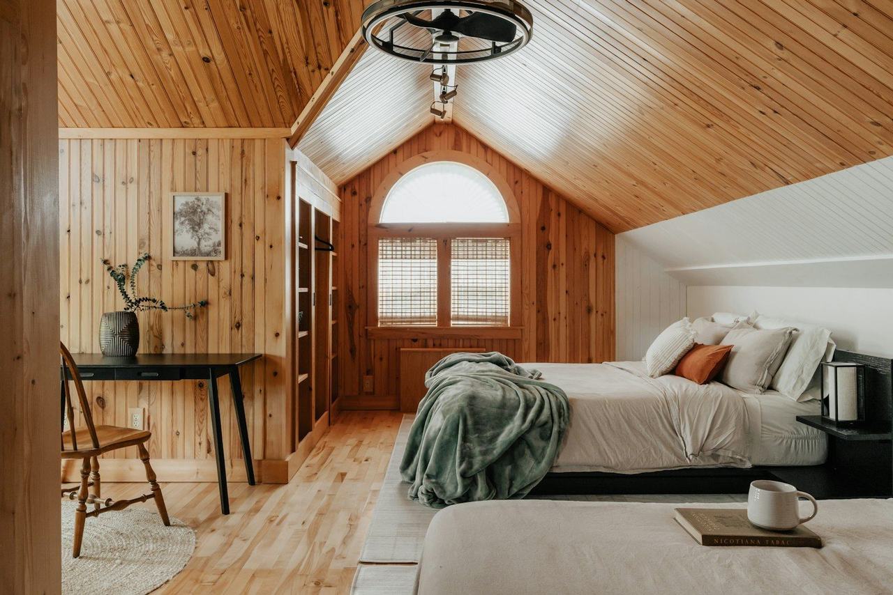 Habitación con revestimiento de lenga, cama y escritorio junto a la ventana